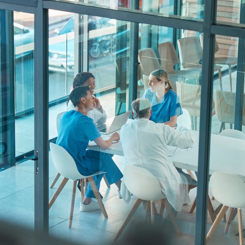 Gesundheitswesen, Ärzte und Teamtreffen mit einem Laptop für eine Diskussion, Planung oder Forschung am Tisch. Männer und Frauen in einer medizinischen Gruppe, die über Kommunikationsstrategien, Viren oder Operationen in einem Krankenhaus sprechen