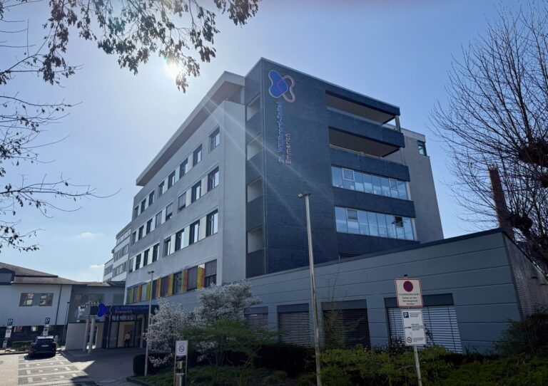 Modern mehrstöckiges Gebäude mit großem blauen Logo und bunten Fahnen am Eingang